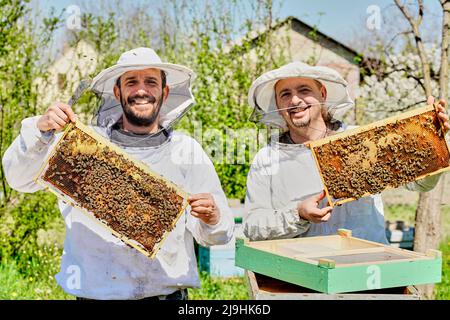 Happy beekeepers wearing protective suit showing honeycomb frame at farm