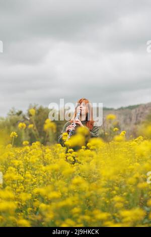 Woman playing clarinet standing in flower field Stock Photo