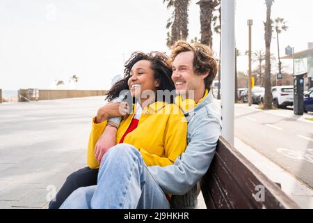 Happy couple sitting on wooden bench at footpath Stock Photo