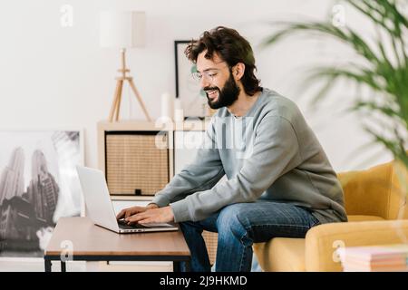 Smiling man wearing eyeglasses using laptop at home Stock Photo