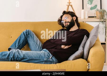Thoughtful bearded man with arms crossed relaxing on sofa at home Stock Photo
