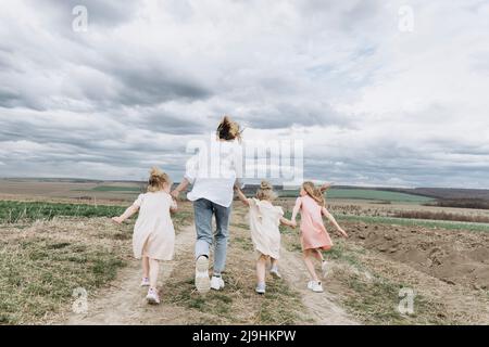 Woman with three daughters running in agricultural field Stock Photo