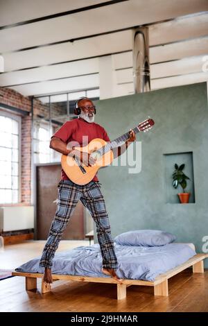 Mature man jumping and playing guitar in bedroom Stock Photo