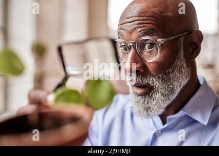 Shocked scientist examining plant with magnifying glass at home Stock Photo