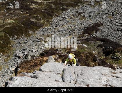 Senior woman wearing helmet climbing rocky cliff on sunny day Stock Photo