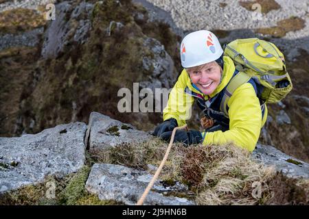 Smiling woman wearing sports helmet climbing rocky mountain Stock Photo