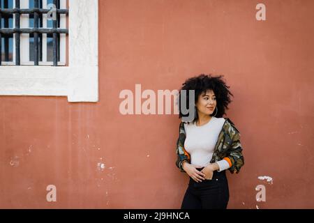 Smiling young woman with hand in pocket standing by wall Stock Photo