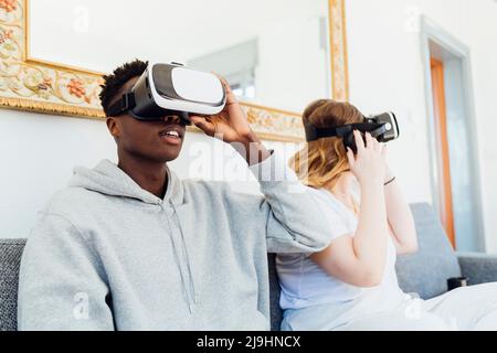 Young couple wearing virtual reality simulators sitting on sofa at home Stock Photo