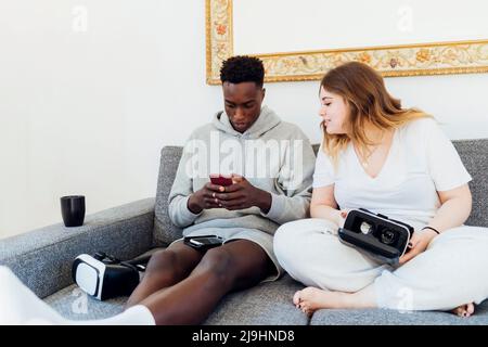 Young man using smart phone sitting by girlfriend on sofa at home Stock Photo