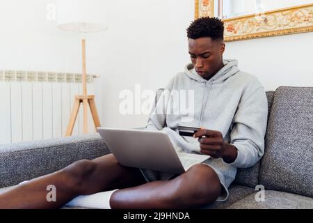 Young man with credit card using laptop at home Stock Photo