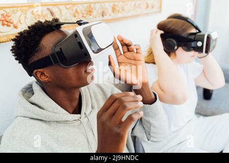 Couple wearing virtual reality simulators sitting on sofa at home Stock Photo