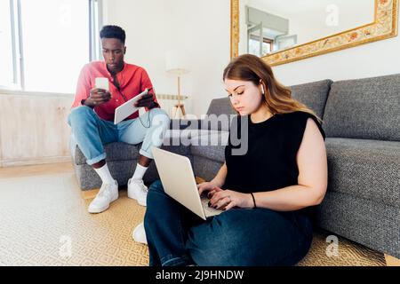 Multiracial couple using laptop and mobile phone in living room at home Stock Photo