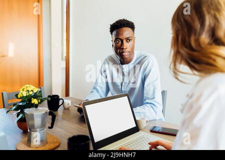 Young woman with laptop sitting by boyfriend at dining table Stock Photo