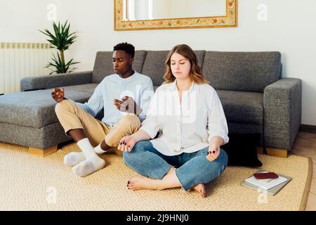 Young couple meditating sitting on carpet in living room at home Stock Photo