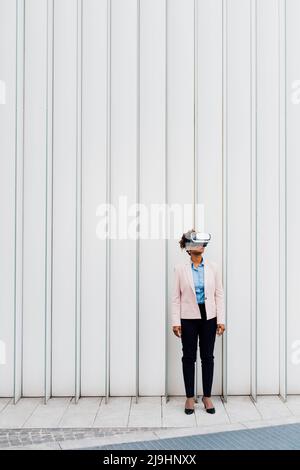 Businesswoman wearing virtual reality simulator in front of white wall Stock Photo