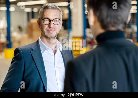 Confident businessman discussing with colleague in warehouse Stock Photo