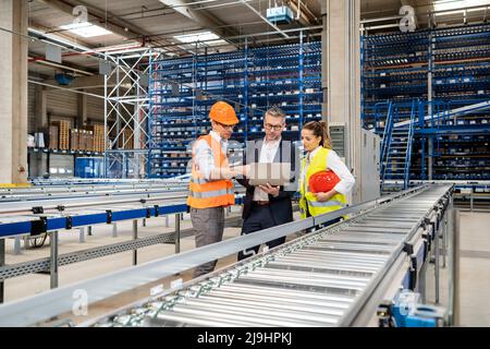 Blue-collar workers discussing over laptop with manager in warehouse Stock Photo