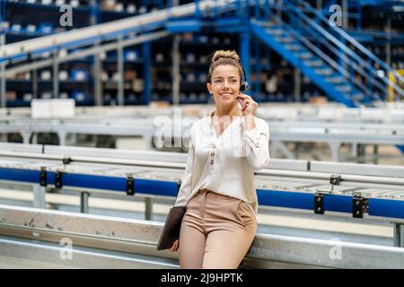 Smiling businesswoman talking on headset in factory Stock Photo