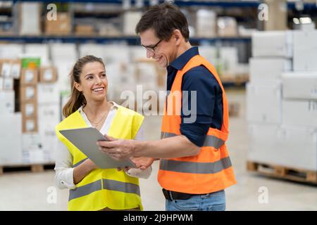 Smiling blue-collar workers discussing over tablet computer in warehouse Stock Photo