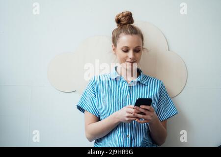 Freelancer using smart phone in front of wall Stock Photo