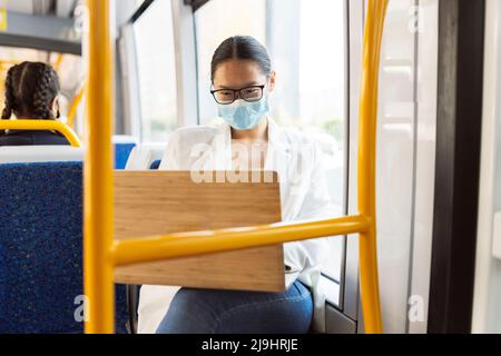 Businesswoman wearing protective face mask using laptop in tram Stock Photo