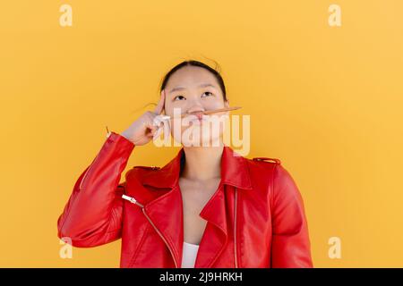 Playful woman with pencil on puckering lips against yellow background Stock Photo