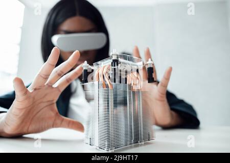 Engineer wearing virtual reality simulator gesturing at machine part on desk Stock Photo