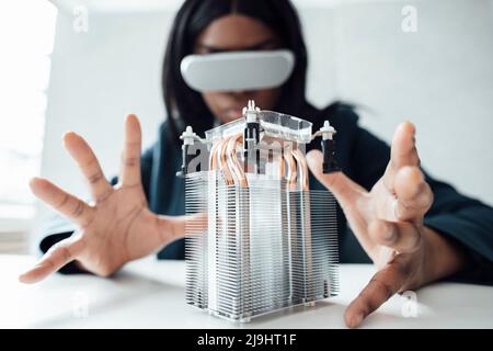 Engineer wearing virtual reality simulator gesturing at semiconductor on desk in office Stock Photo