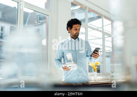 Businessman holding drone remote control using smart phone in front of window at office Stock Photo