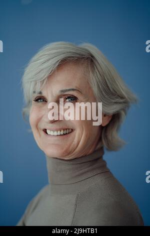 Happy senior woman with gray hair against blue background Stock Photo