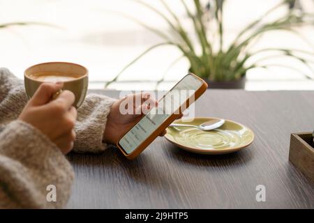 Hands of woman holding coffee cup using mobile phone in cafe Stock Photo
