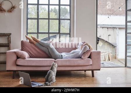 Woman lying on sofa by window in living room at home Stock Photo