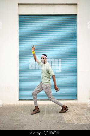 Playful man dancing on footpath in front of blue shutter Stock Photo