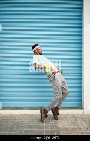 Flexible man dancing on footpath in front of blue shutter Stock Photo