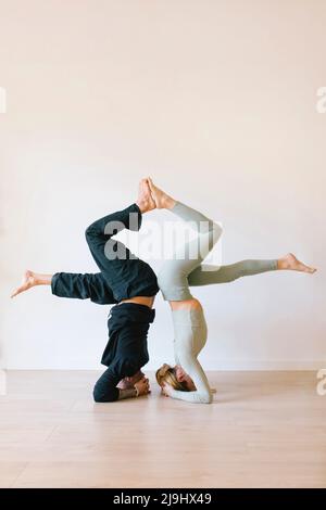 Man and woman practicing headstand in front of wall at yoga studio Stock Photo
