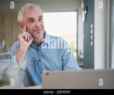 Thoughtful freelancer with laptop sitting at home Stock Photo