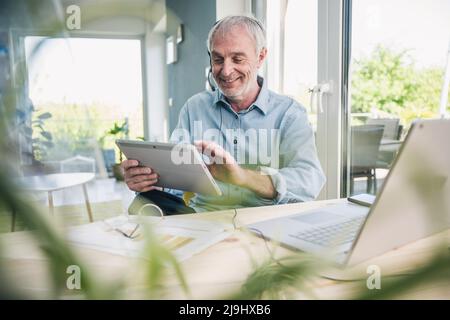 Smiling freelancer wearing headset using tablet PC at home Stock Photo