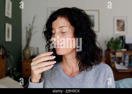 Woman smelling essential oil from bottle at home Stock Photo