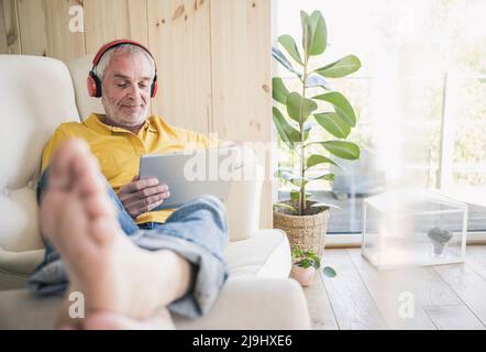 Senior man wearing wireless headphones using digital tablet at home Stock Photo