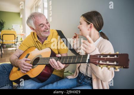 Happy senior man playing guitar by granddaughter at home Stock Photo