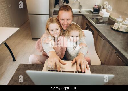 Happy businessman with daughters using laptop in kitchen at home Stock Photo