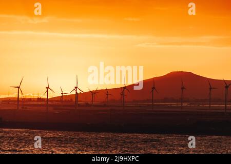 Silhouette wind turbines in front of mountain at sunset Stock Photo