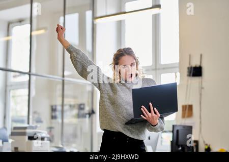 Tired young woman in office holding laptop and yawning Stock Photo
