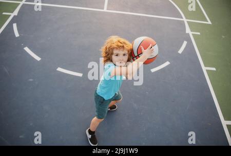 Cute smiling boy plays basketball. Active kids enjoying outdoor game with basket ball, Top view. Stock Photo