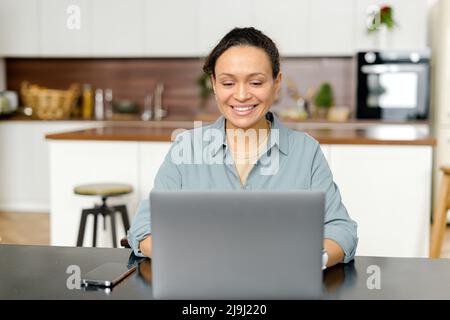 Focused female office worker sitting at the desk at the kitchen, working on project, typing on the laptop, concentrated on clients problem Stock Photo
