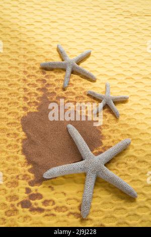 Vertical shot of three starfish and sand from a beach on a yellow background. Copy space. Stock Photo