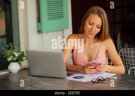 Web Designer remote working concept.Successful stylish female tourist working at modern laptop computer sitting at a table in coffee shop cafe Stock Photo
