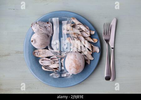 Blue plate with dried and colored exotic fruits, empty glass goblet and cutlery on a wooden table Stock Photo