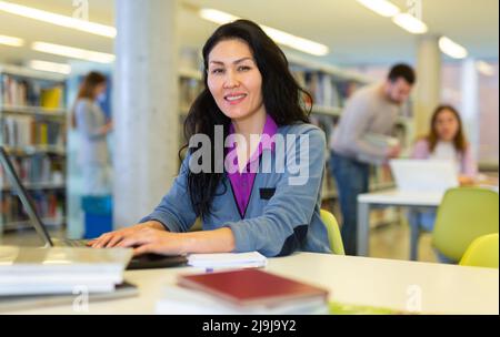 Focused woman working on laptop at library Stock Photo