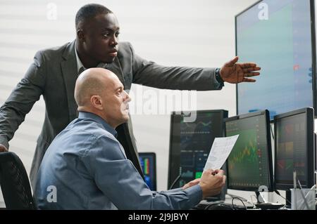 Two ethnically diverse stock trading specialists working with data looking at monitor screen and analyzing future results Stock Photo